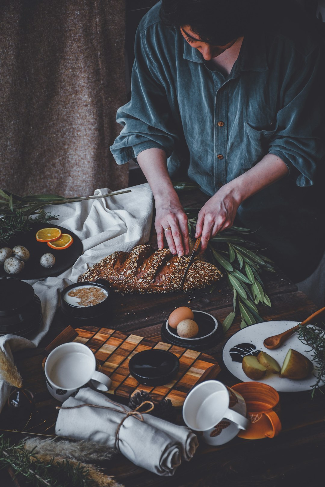 Moody dark photo of a rustic wooden table with bread and herbs